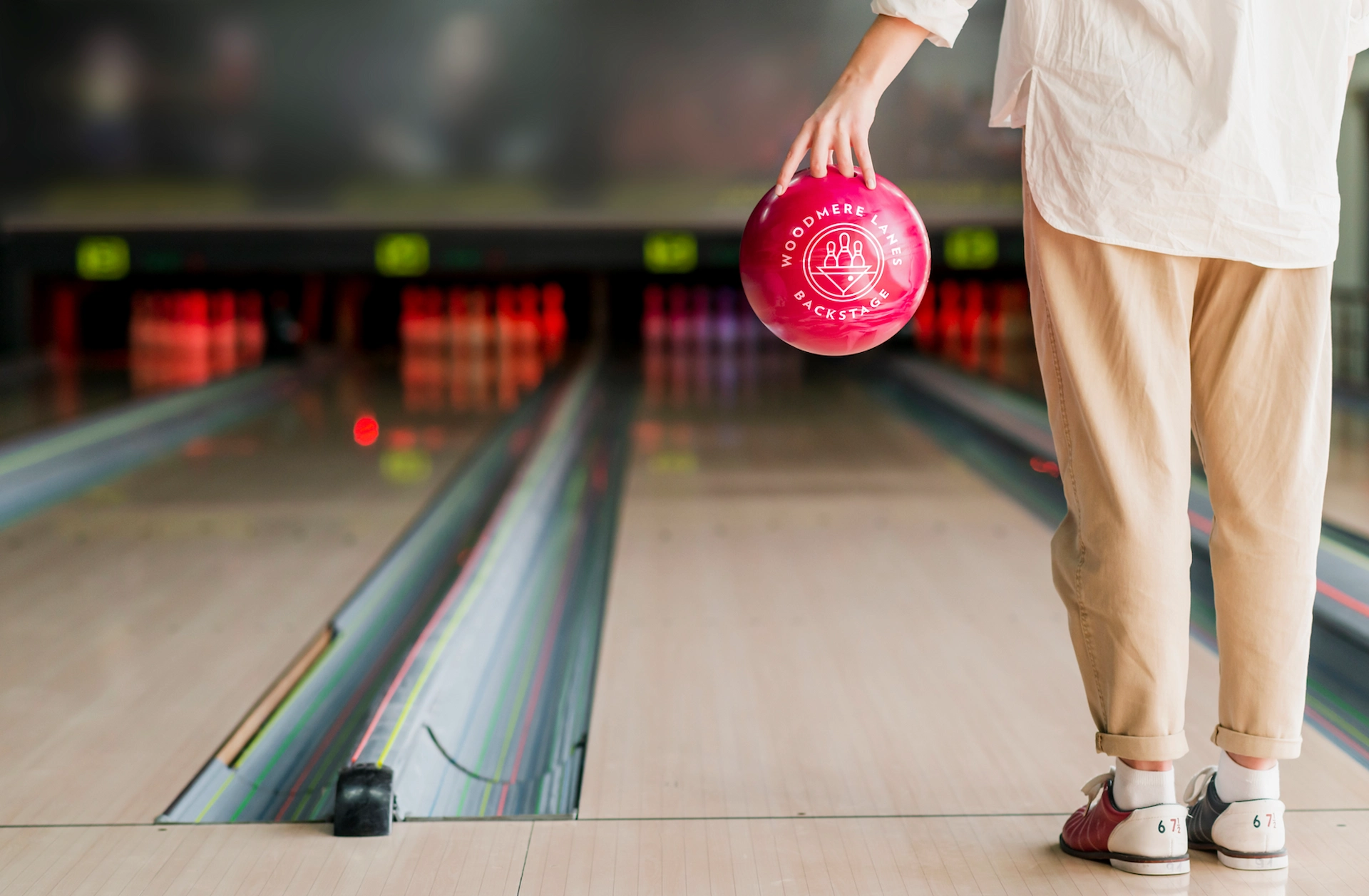 Bowler holding a pink Woodmere Lanes ball at the foul line, lanes stretching ahead